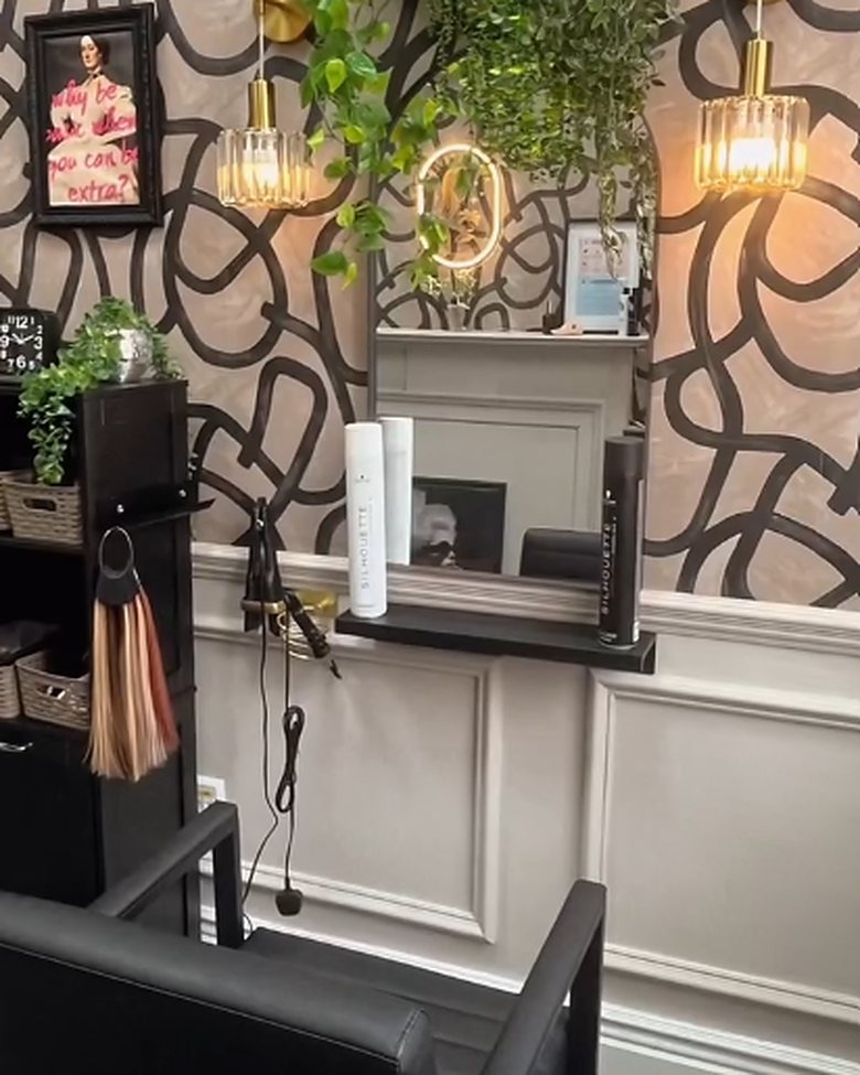 A styling station at Beaux Cheveux: the salon's black-swirl wallpaper, gold glass pendant lights, a fitted mirror shelf and a colour-match ring of hair shades.