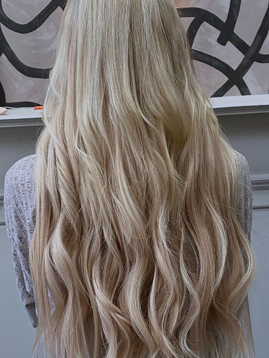 After: the same client photographed from behind again, now with waist-length blonde waves in a blend of light bleach blonde and cool honey blonde.