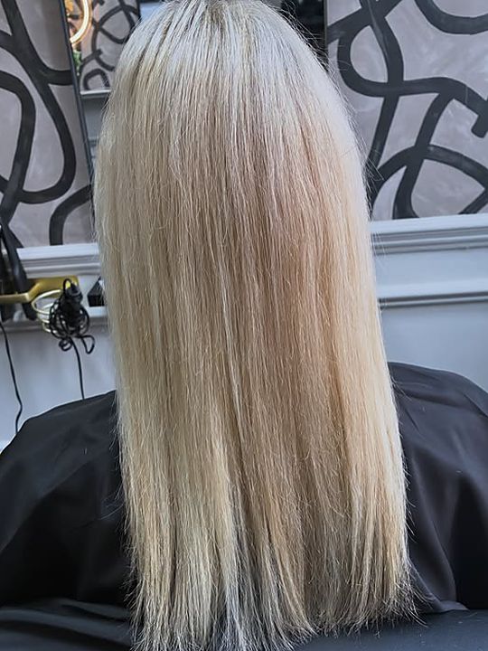Before: a client's own bleach-blonde hair, straight and shoulder-length, photographed from behind in the salon.